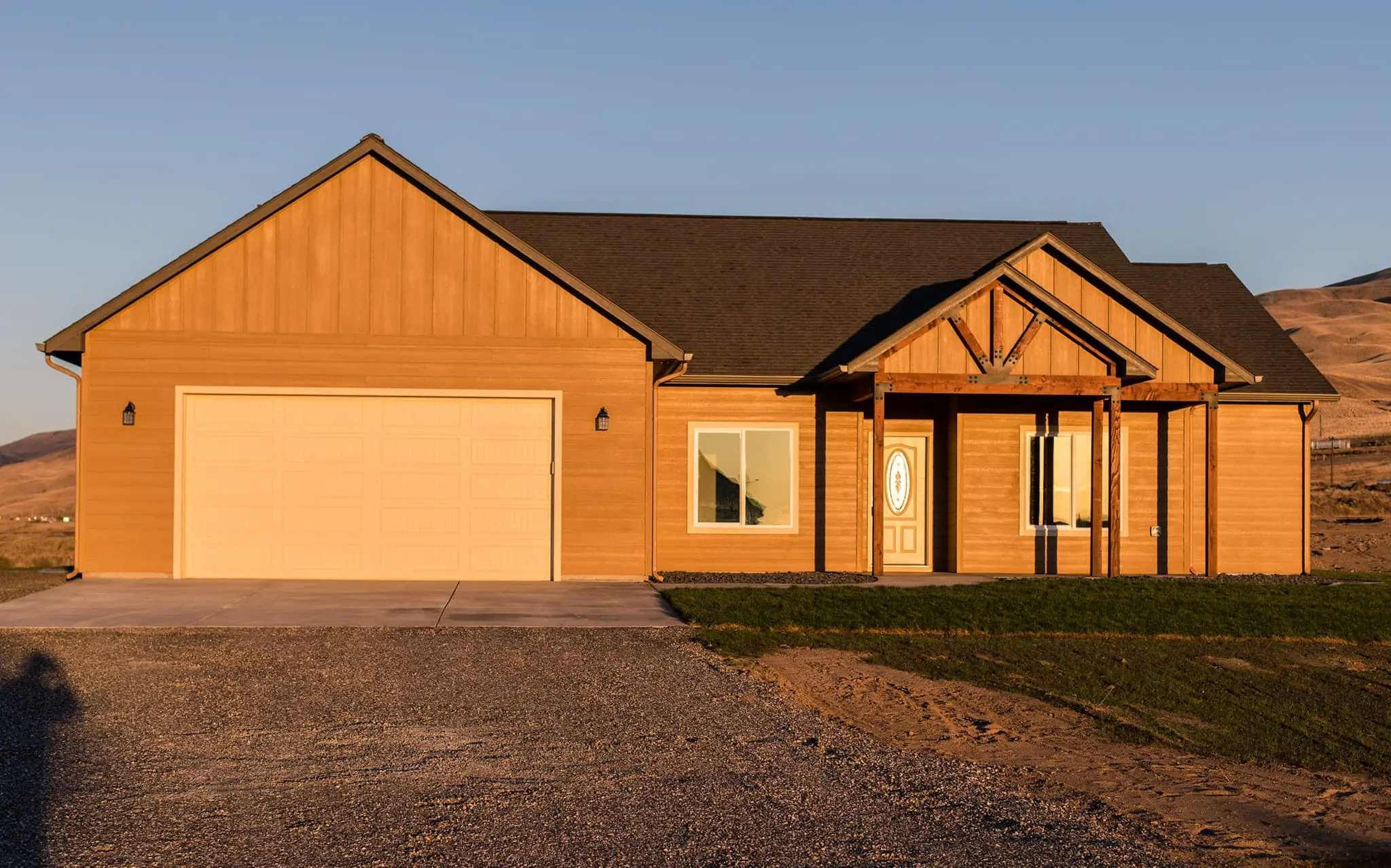 Exterior of a completed custom ranch-style home by Anasazi Builders featuring a prominent timber-framed entry porch, warm wood siding, and golden-hour lighting in a mountain landscape.