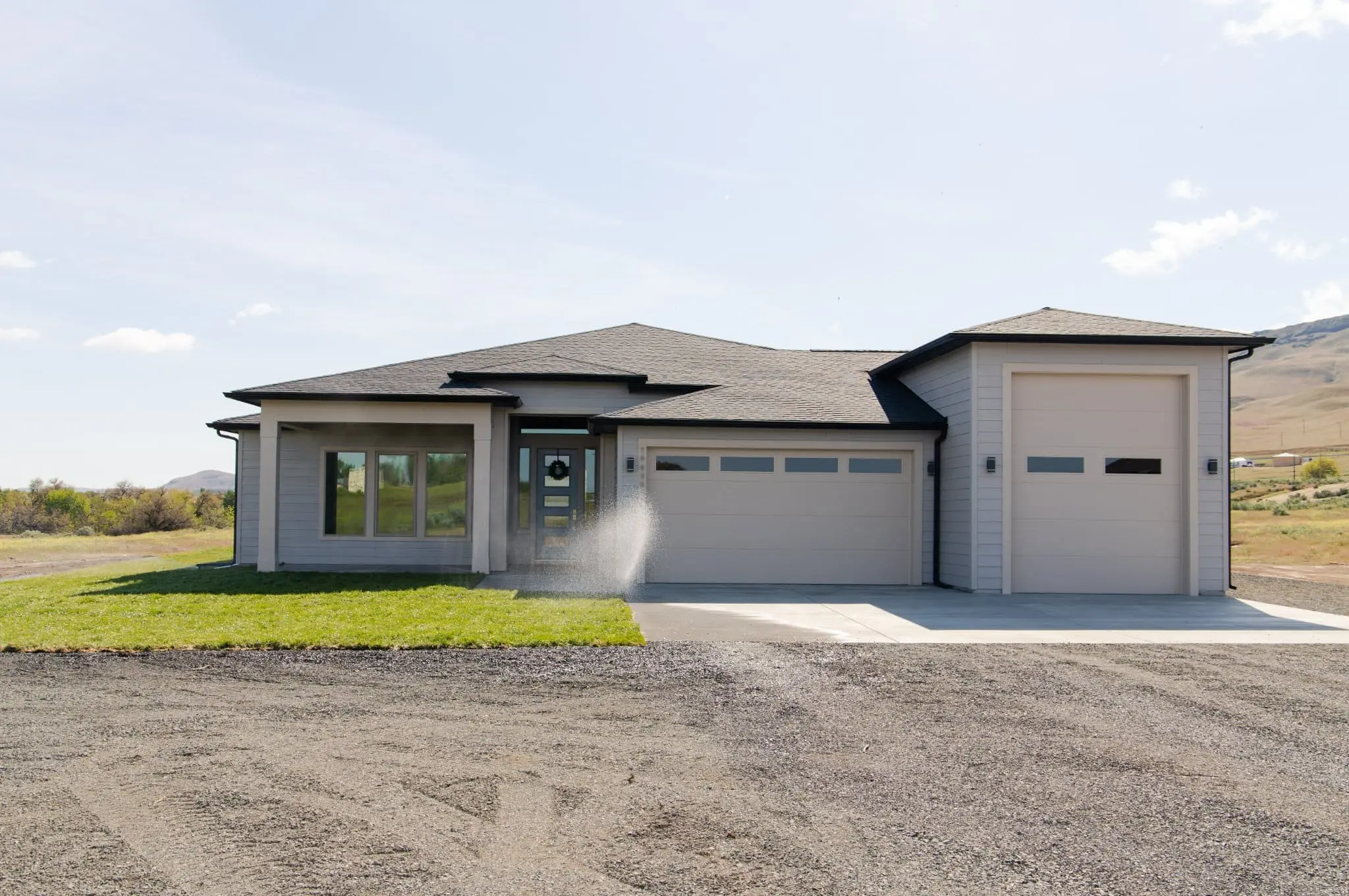 Exterior view of a modern luxury custom home completed by Anasazi Builders in Idaho, featuring a sleek gray facade, professional landscaping, and a high-clearance RV garage.
