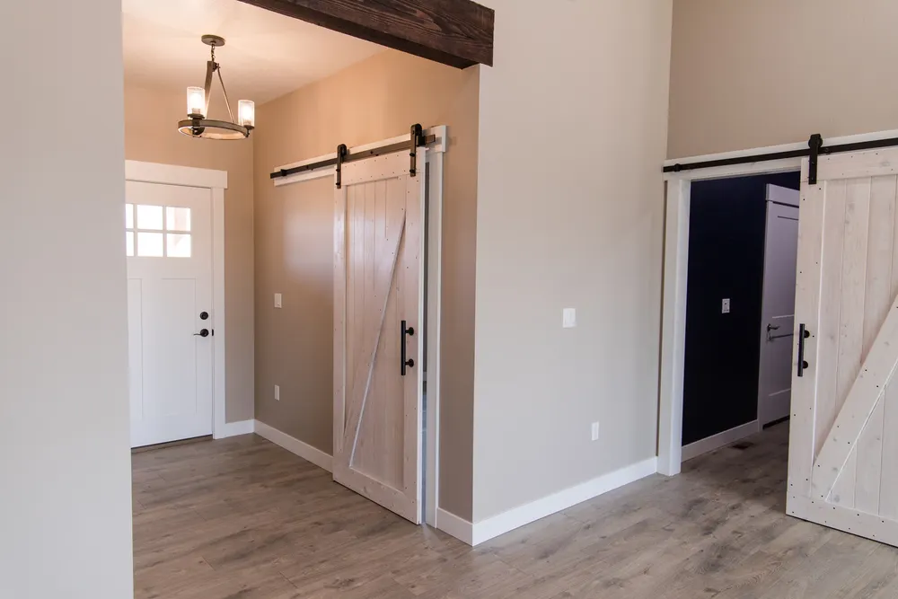 Interior entryway of a modern home featuring two white wooden sliding barn doors with black hardware and a white craftsman-style front door, installed by Anasazi Builders in Benton County, WA