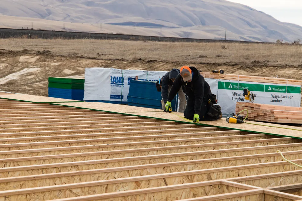 A professional contractor from Anasazi Builders working on the floor joists of a new custom home in Tri-Cities with a desert mountain background.