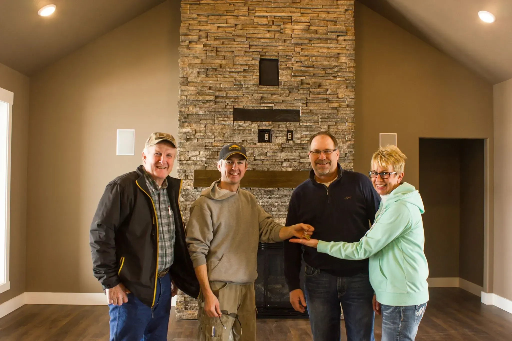 Anasazi Builders team handing over keys to new homeowners in front of a custom stacked stone fireplace in Tri-Cities.