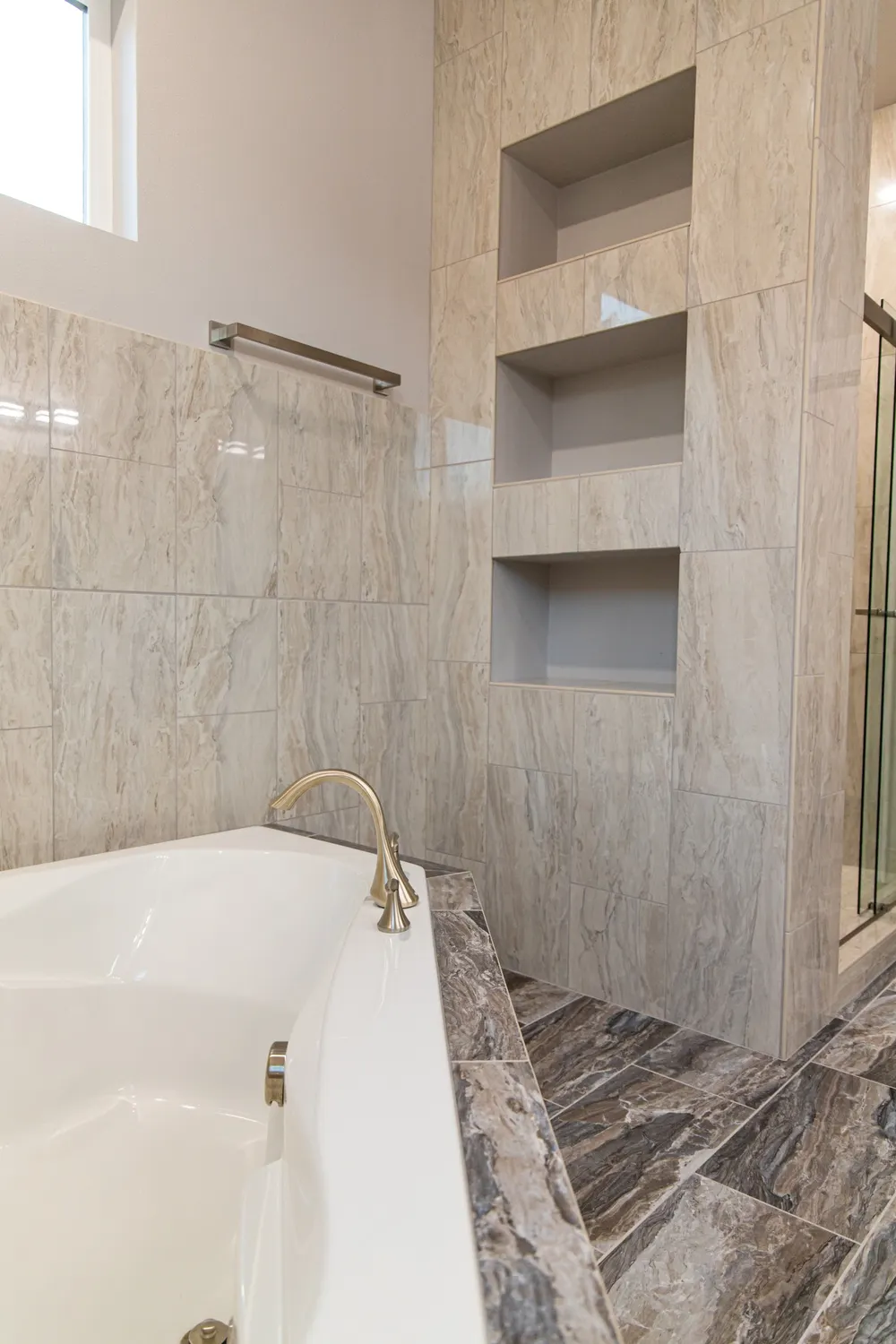 Luxurious master bathroom featuring a white soaking tub with gold fixtures and a custom-tiled wall with integrated storage niches, by Anasazi Builders in Tri-Cities.