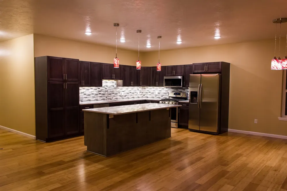 Large modern kitchen with dark espresso cabinets, a white speckled quartz island, stainless steel appliances, and vibrant red glass pendant lights, by Anasazi Builders in Tri-Cities.