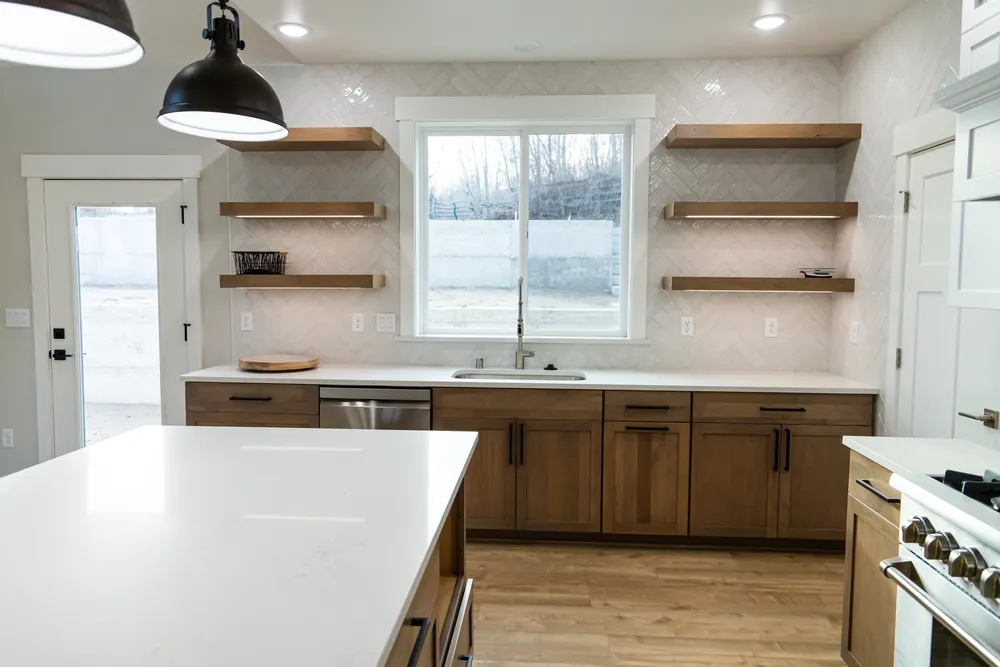 A modern kitchen featuring natural wood lower cabinets, white quartz countertops, and white herringbone tile backsplash with floating wood shelves, completed by Anasazi Builders in Tri-Cities.