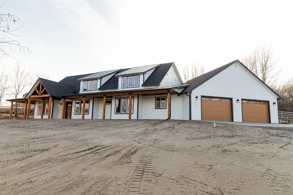 A wide-angle view of a modern open-concept great room featuring a kitchen with a natural wood island and white quartz countertops, black industrial pendant lights, and a living area with a vaulted ceiling and loft overlook, built by Anasazi Builders in Tri-Cities.