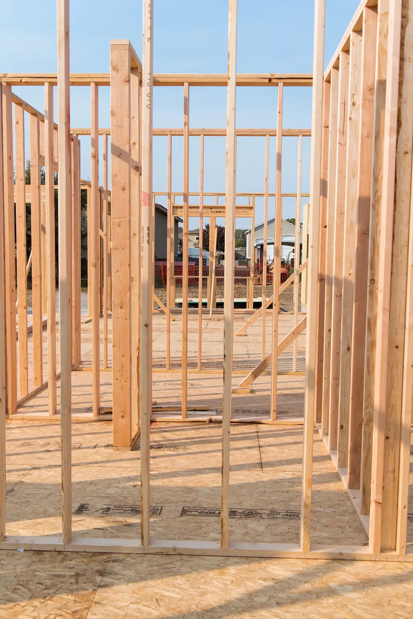 Interior view of a custom home under construction showing wood wall framing and OSB subflooring on a sunny day.