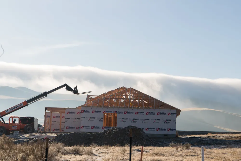 Professional builder from Anasazi Builders standing on floor joists at a Tri-Cities custom home site with scenic hills.