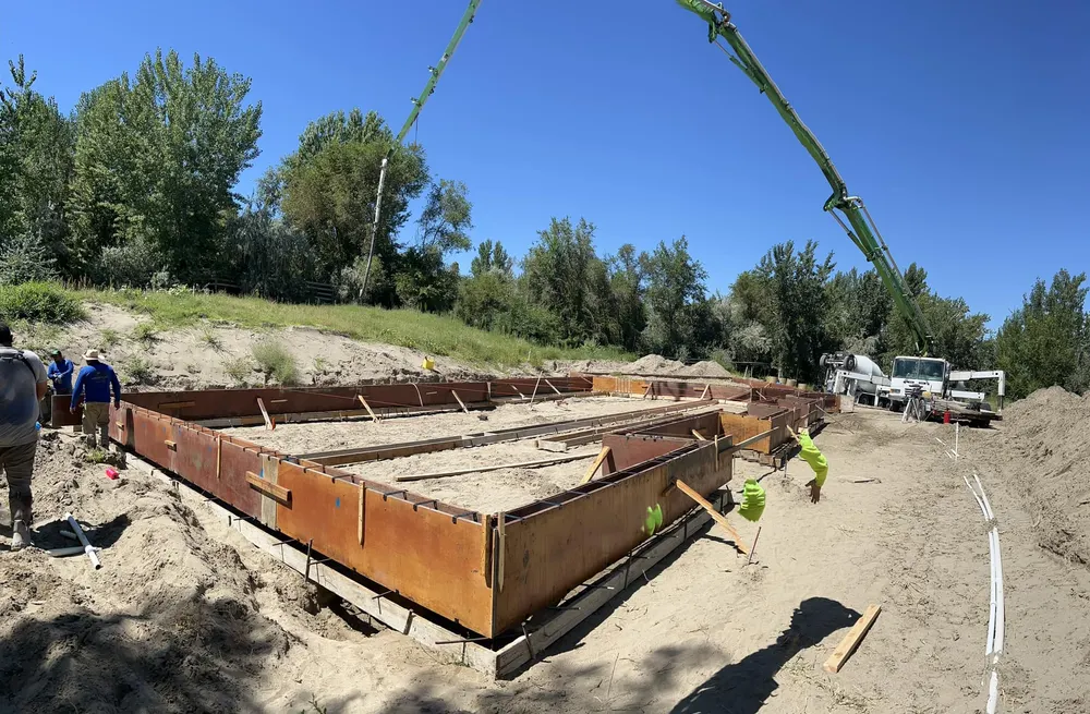 Construction crew and a concrete pump truck pouring the foundation for a new custom home in West Richland on a sunny day.