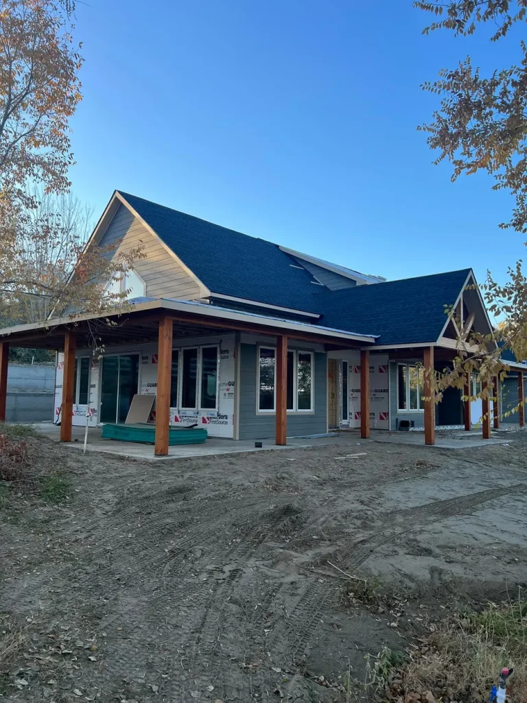Exterior of an Anasazi Builders custom home in West Richland featuring a dark shingle roof, grey siding, and large covered porches with natural wood pillars.