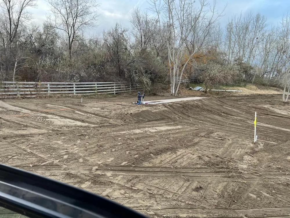 Wide view of a large residential lot in West Richland being graded and leveled by Anasazi Builders with a construction worker in the distance.