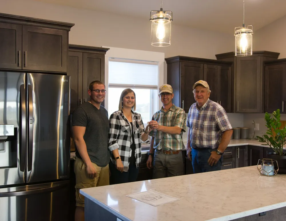 Anasazi Builders founders John and Stephen handing over the keys of a newly built custom home to smiling clients in their modern Benton County kitchen.